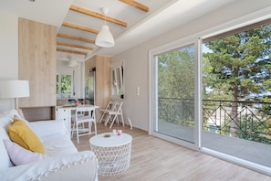 A modern living room with a sofa, a dining table, and a balcony with a view of trees.