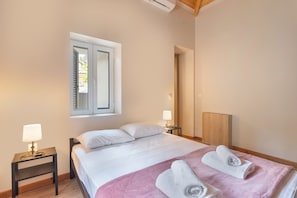 A bedroom with a bed, two bedside tables, a window, and a wooden headboard.