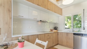 Une cuisine moderne avec des meubles blancs, un plan de travail en bois, une table à manger avec des chaises et un lave-vaisselle.