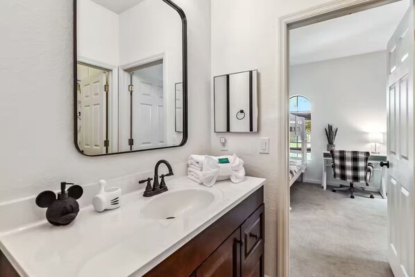 A modern bathroom with a white vanity, a large mirror, a black faucet, and a towel rack.