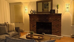 A living room with a brick fireplace, a sofa, a coffee table, and wall-mounted sconces. - Spacious 4-bedroom house in charming West Tisbury (West Tisbury)