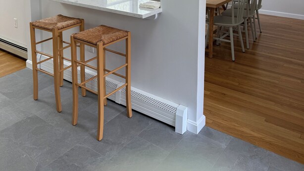 A modern kitchen with a white countertop, two wooden stools, a window with a view of greenery, and a dining area with a wooden table and chairs. - Spacious 4-bedroom house in charming West Tisbury (West Tisbury)