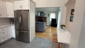 A modern kitchen with white cabinets, a stainless steel refrigerator, and a dining area with a white countertop and wooden chair. - Spacious 4-bedroom house in charming West Tisbury (West Tisbury)