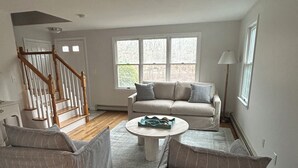 A spacious living room with a wooden staircase, a beige sofa, and a coffee table. - Spacious 4-bedroom house in charming West Tisbury (West Tisbury)