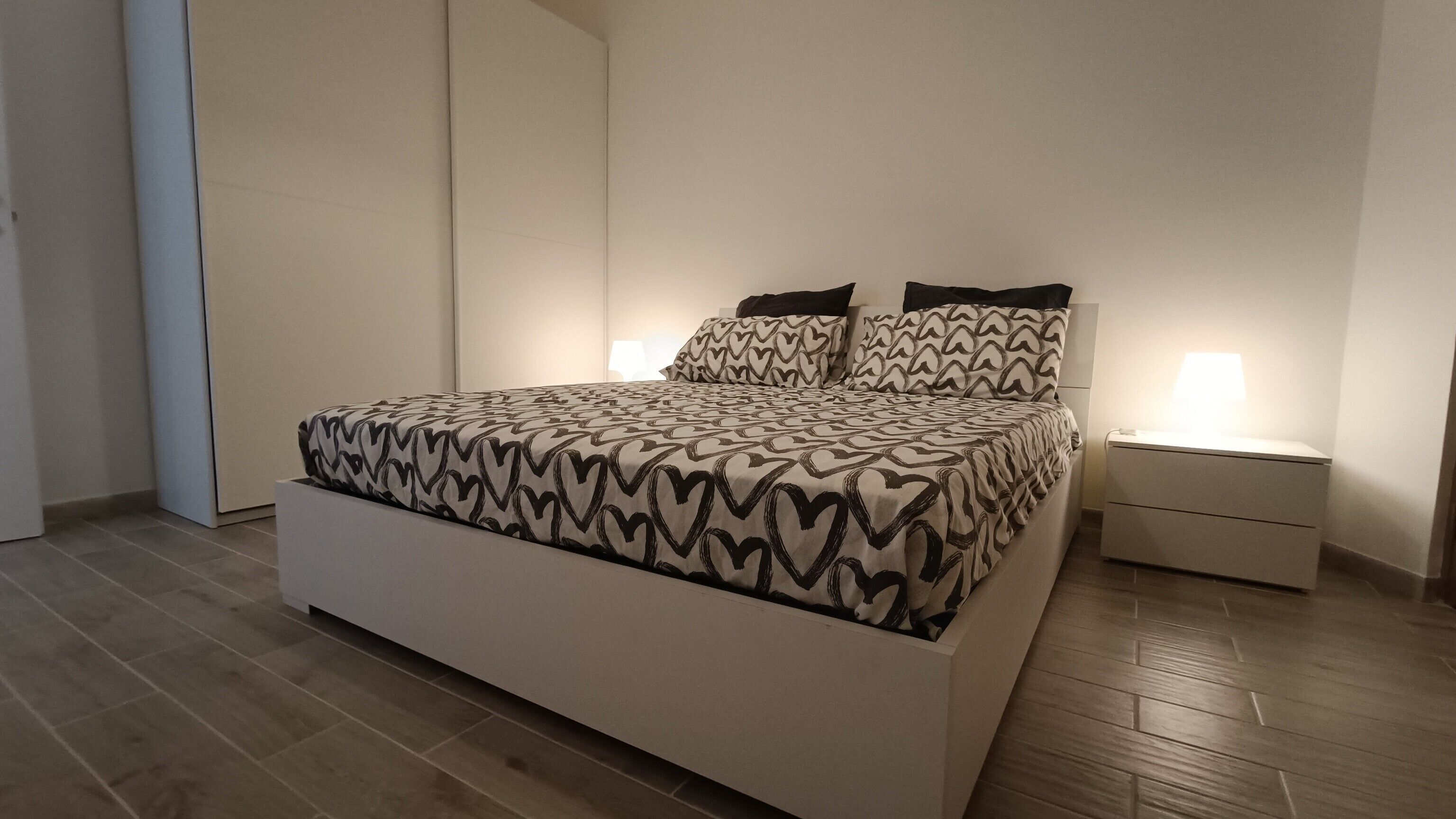 Een moderne slaapkamer met een groot bed, twee nachtkastjes en een bedbank.