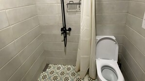 A small bathroom with a shower, toilet, and patterned floor tiles. - House in the Vineyard (Ambrolauri)