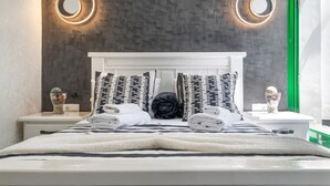 A neatly made bed with a white headboard, two bedside tables with decorative items, and a wall with circular light fixtures. - Vacation Apartment 'Onyx' with Sea View, Wi-Fi and Air Conditioning (Puerto del Carmen)