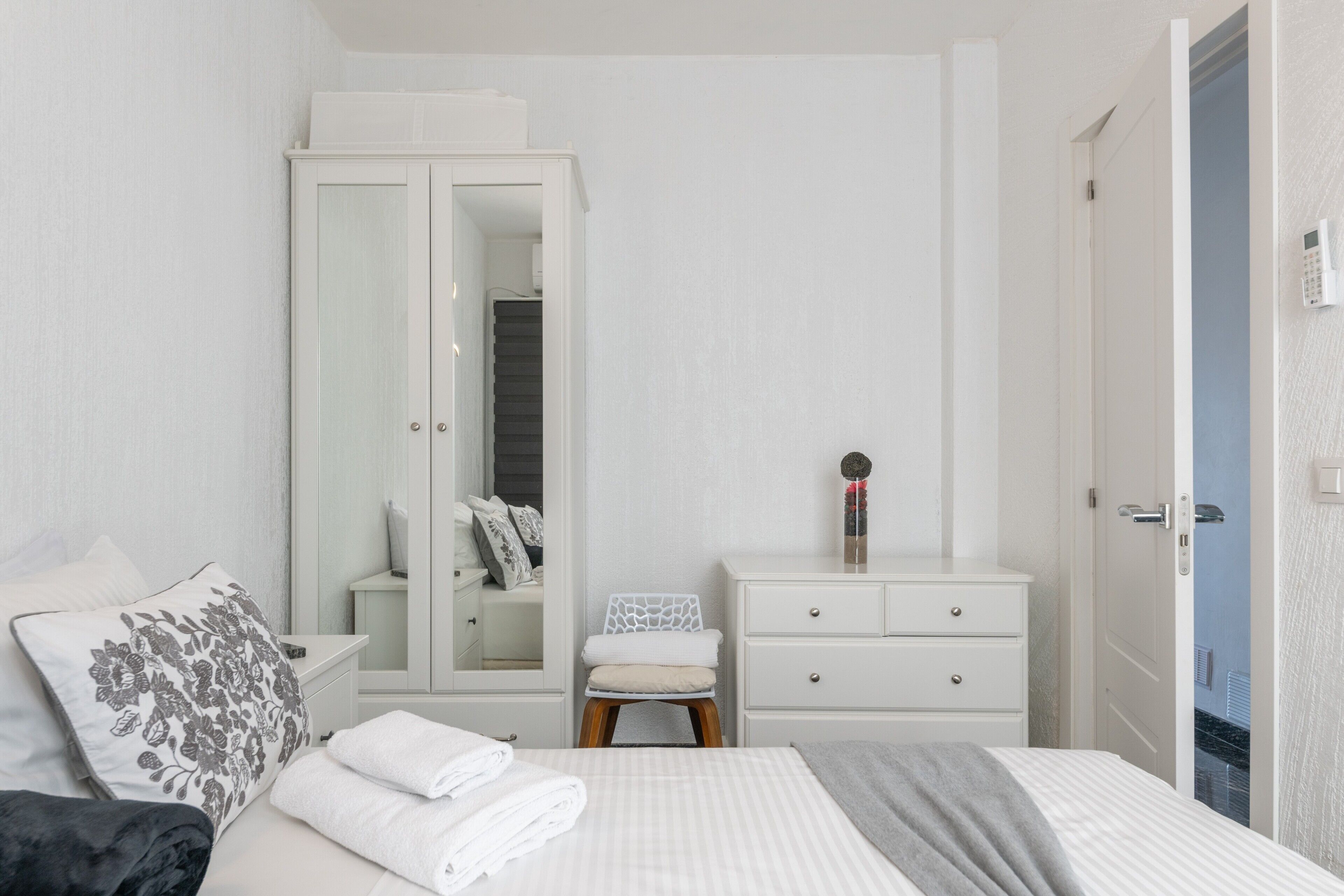 A bedroom with a bed, a wardrobe, a chair, a dresser, and a door.