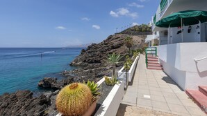 A coastal building with a paved walkway, a cactus, and a view of the sea. - Vacation Apartment 'Onyx' with Sea View, Wi-Fi and Air Conditioning (Puerto del Carmen)