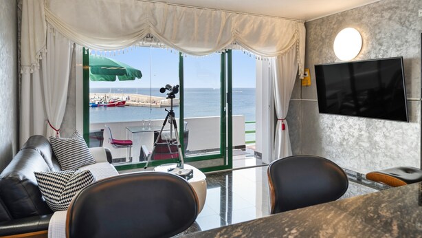 A modern living room with a sofa, chairs, a TV, and a view of the sea. - Vacation Apartment 'Onyx' with Sea View, Wi-Fi and Air Conditioning (Puerto del Carmen)
