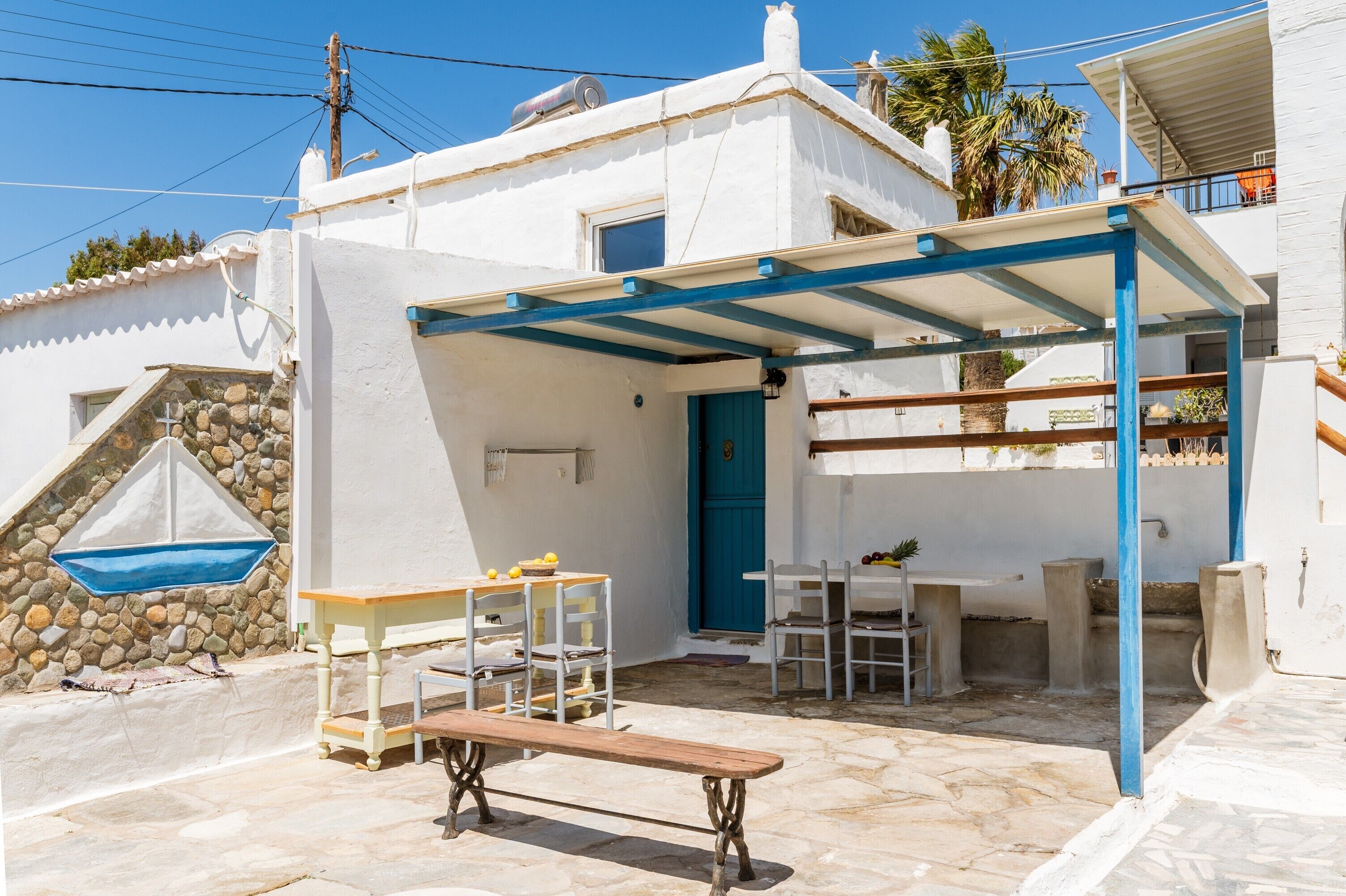 A white building with a blue door, outdoor seating, and a stone wall.