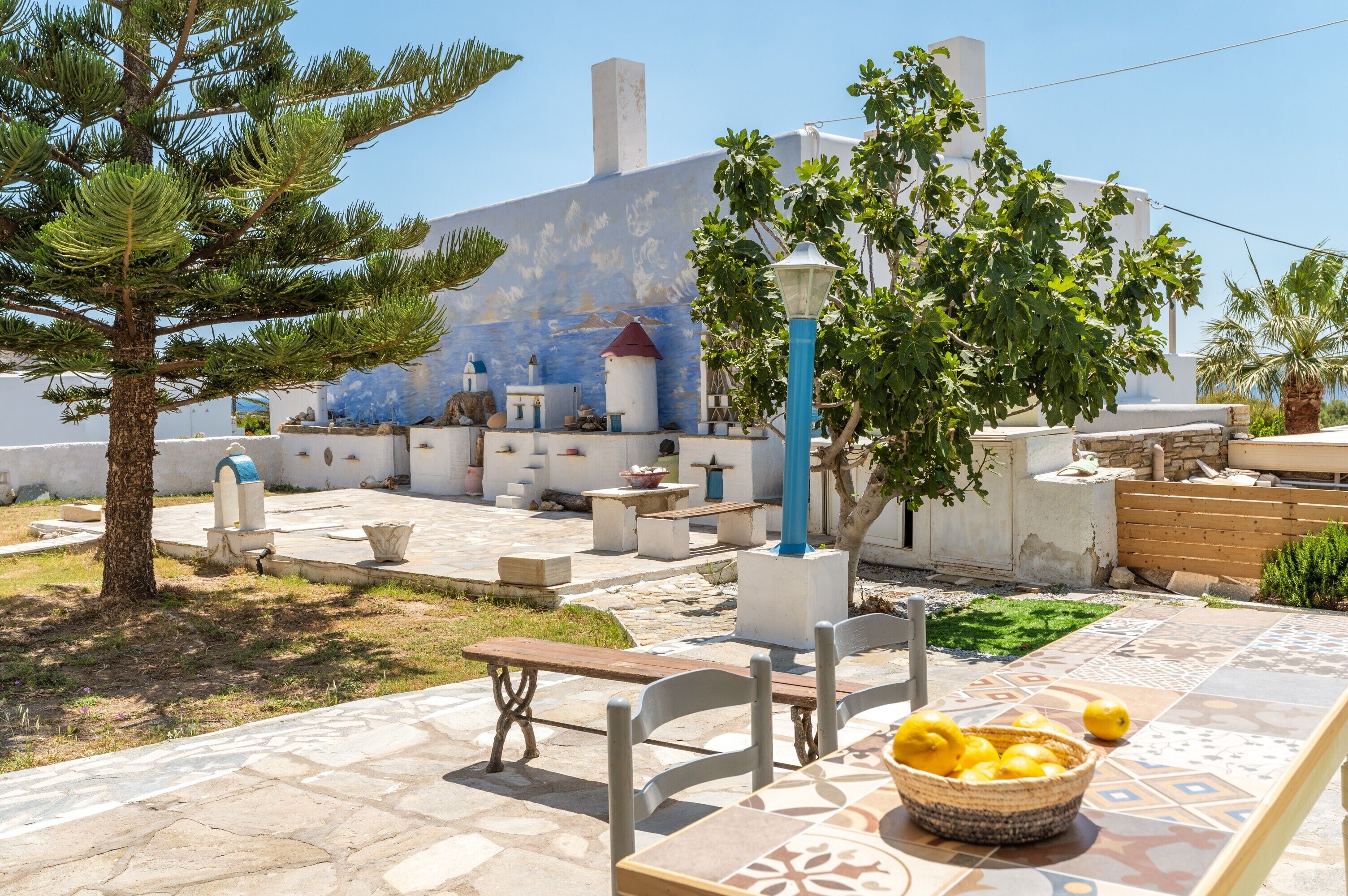 An outdoor patio area with stone flooring, a table with a basket of lemons, and a building with a blue and white facade in the background.