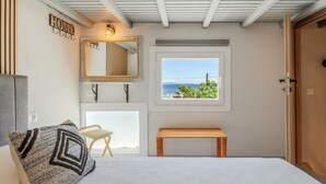 Ein Schlafzimmer mit Bett, einer Bank, einem Stuhl, einem Fenster mit Aussicht und einem Spiegel, sowie einem Schild mit der Aufschrift 'HOME'.