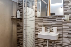 A modern bathroom with a tiled wall, a sink with two bottles, and a mirror.