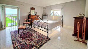 Un dormitorio con cama, cómoda, silla, ventana grande y vista al exterior.