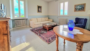 Una sala de estar con un sofá beige, una mesa de centro de madera, un jarrón azul y una alfombra estampada.