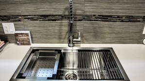 A modern kitchen with a stainless steel sink, a built-in trash can, and a backsplash with a wood-like pattern. - Home away from home (Grande Prairie)
