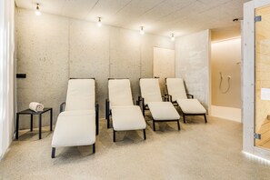 Une pièce comprenant quatre fauteuils inclinables, une petite table avec une serviette et une porte en bois donnant accès à un espace douche.