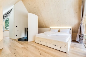 A bedroom with a sloped ceiling, a bed with white bedding, and a wooden floor.