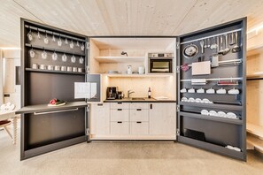 Una cocina compacta con microondas, cafetera y varios utensilios en estantes.