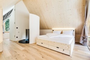 Ein Schlafzimmer mit schrägemaßtem Dach, einem Bett mit weißer Bettwäsche und Holzboden.