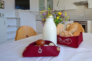 Une table à manger ornée d’un vase de fleurs, d’un panier à pain et d’un tissu rouge sur lequel sont posés des œufs.