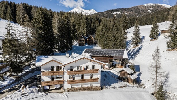 A snow-covered mountain village with wooden buildings, a ski slope, and a solar panel installation.