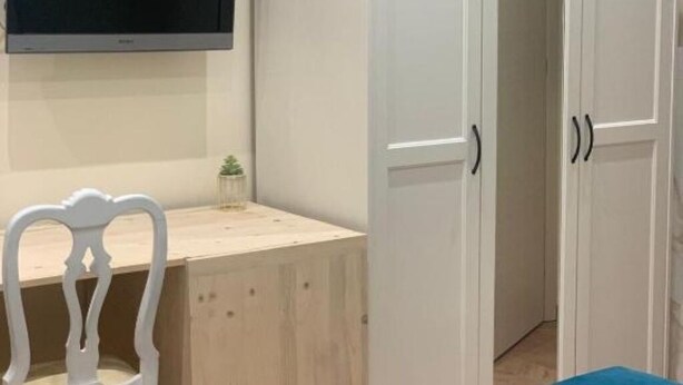 A room with a television mounted on the wall, a wooden desk with a chair, and white wardrobes. - Guest house that's love rome (Roma)