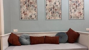 A room with a white upholstered bench against a light blue wall, adorned with three abstract paintings and several cushions. - Guest house that's love rome (Roma)