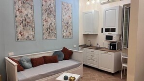 A compact living space with a sofa, a small table, and a kitchenette. - Guest house that's love rome (Roma)