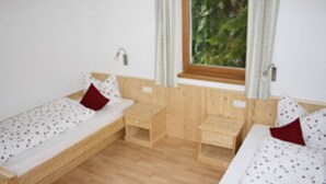 Eine kleine, einfache Unterkunft mit zwei Holzbetten, einem Fenster mit Vorhängen und Holzdielen.
