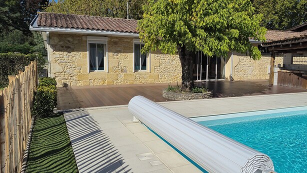 A stone house with a swimming pool, wooden deck, and a pergola.