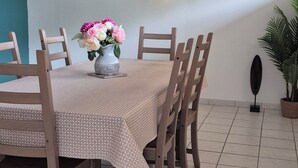 A dining area with a round table, wooden chairs, a vase of flowers, a wall clock, and a wall-mounted light fixture.