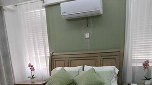 Ein ordentlich bezogenes Bett mit einer grünen Tagesdecke, zwei Kissen und gerollten Handtüchern auf einem hölzernen Bettgestell.