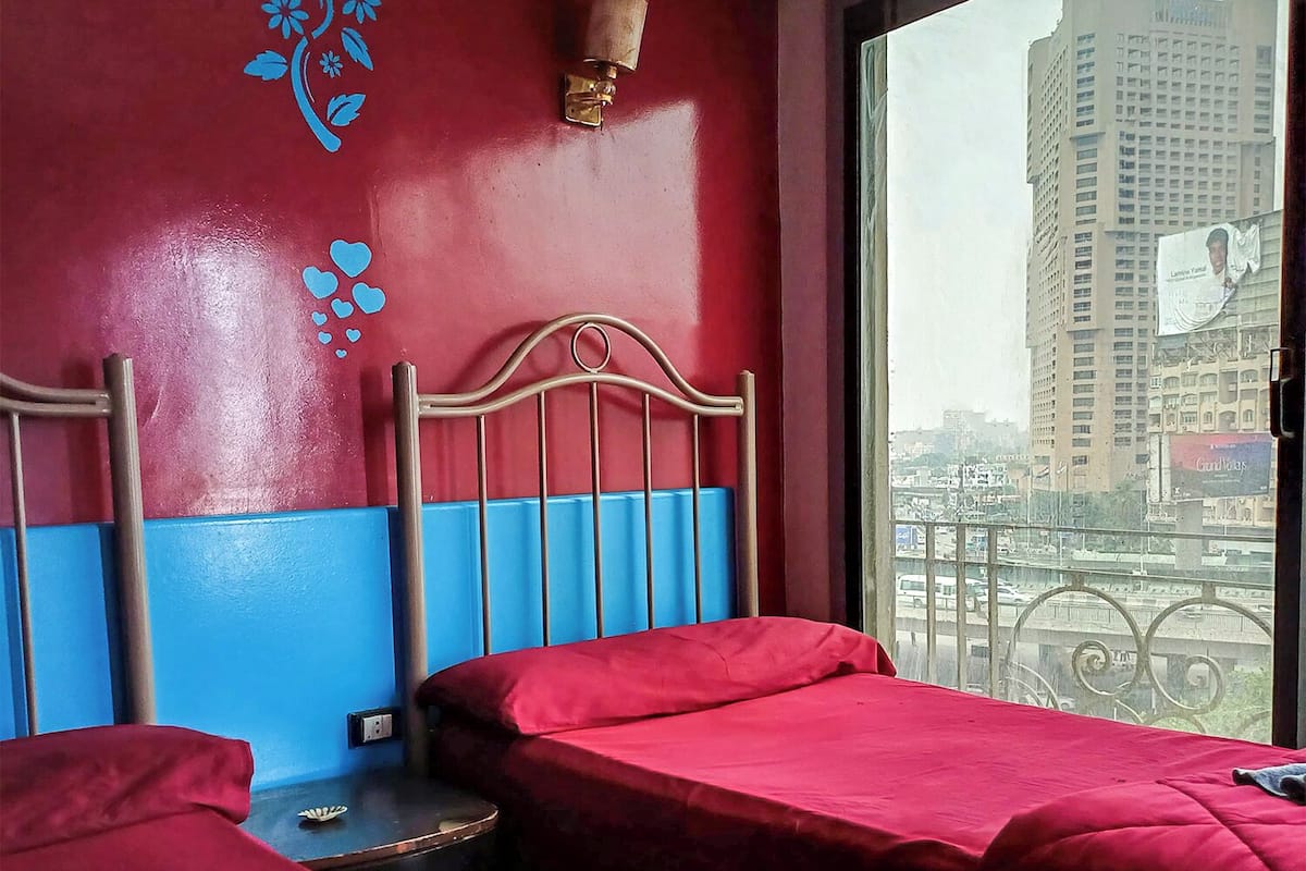 Una habitación de hotel con dos camas, un ventanal con vista a la ciudad y un muro decorativo.