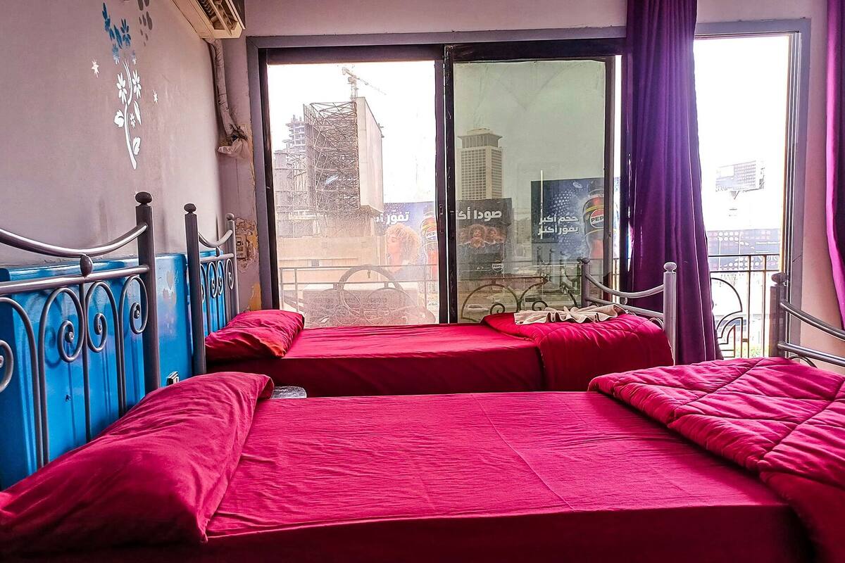 Una habitación con dos camas, un ventanal con vistas a la ciudad y un balcón con una bicicleta.