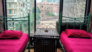 A room with two beds, a small table, and a view of buildings and a construction site through large windows. - OASIS Hotel Downtown (Cairo)