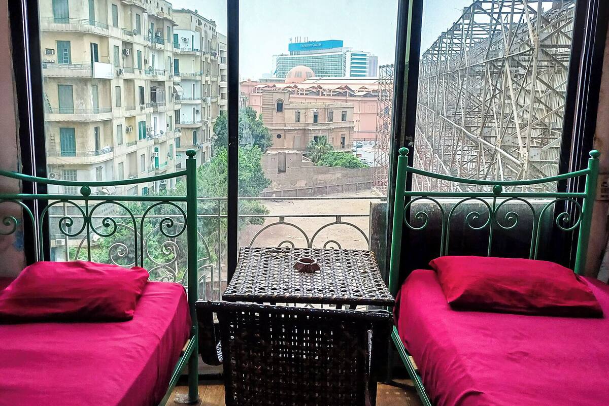 Una habitación con dos camas, una mesita y vistas a edificios y una obra en construcción a través de amplias ventanas.
