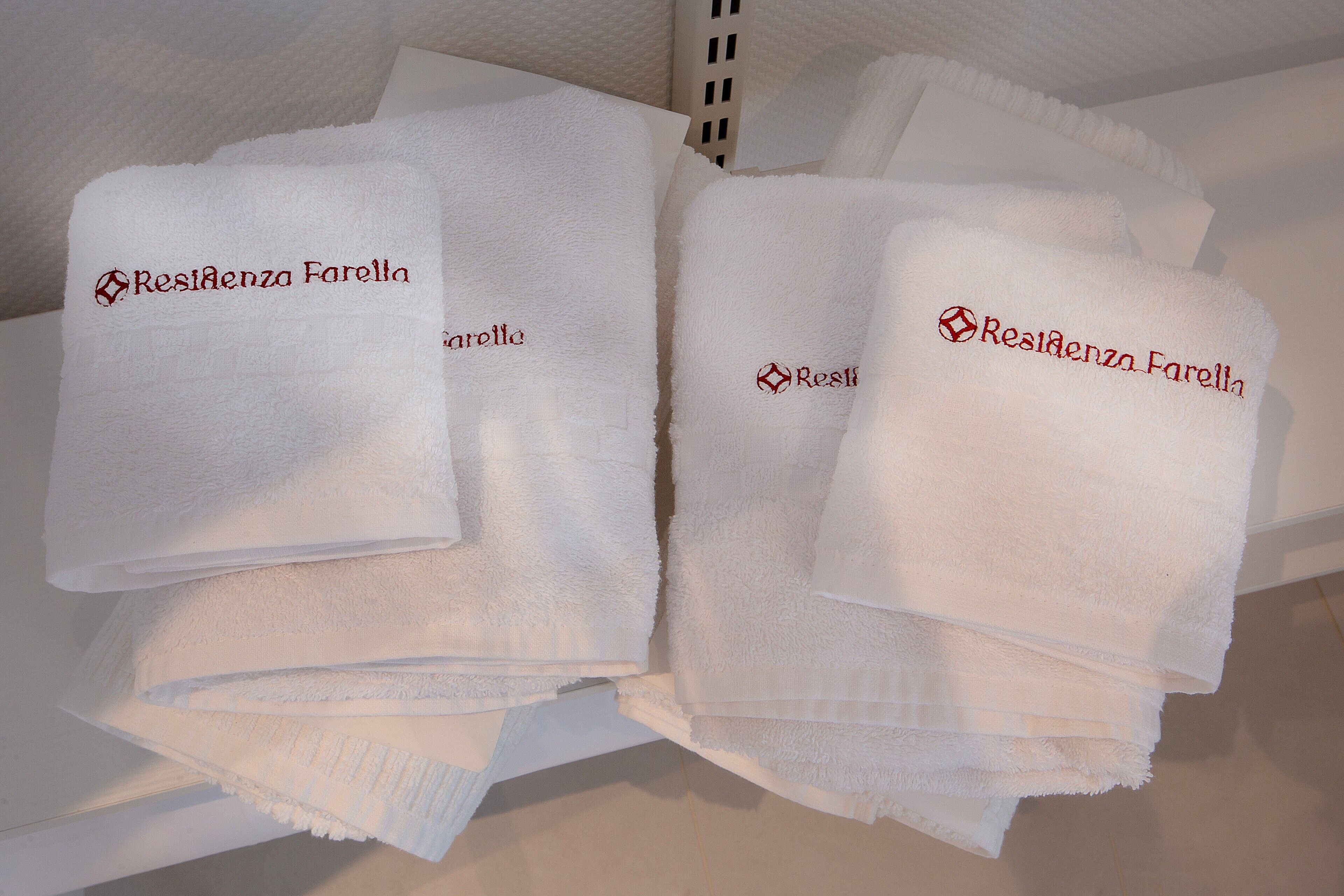 A stack of white towels with embroidered text 'Residenza Farella' on a white surface.