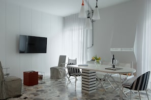 A modern dining area with a white table, striped chairs, a flat-screen TV mounted on the wall, and a stone-patterned floor.