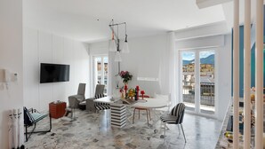 A spacious living area with a dining table, chairs, a sofa, a TV, and a balcony with a city view.