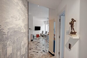 Un pasillo con un papel tapiz estampado, una estatua y un televisor fijado a la pared.