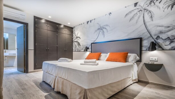 Une chambre moderne avec deux lits, une grande armoire et une fresque murale aux motifs tropicaux.