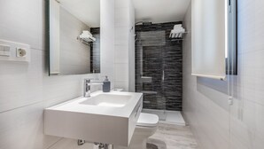 Une salle de bain moderne avec un lavabo blanc, des toilettes et une douche séparée par une paroi de verre.