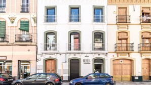 A row of three-story buildings with balconies, a restaurant named "Mecella" on the ground floor, and parked cars in front. - Superior Suite - Open Space (Sevilla)