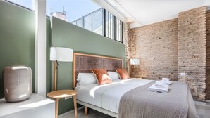 A modern bedroom with a large bed, a small side table, and a brick wall.