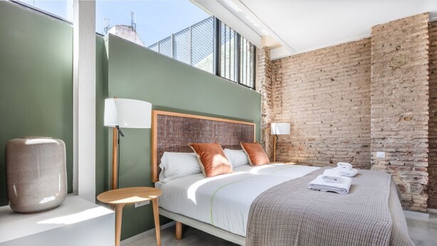 A modern bedroom with a large bed, a small side table, and a brick wall. - Superior Suite - Open Space (Sevilla)