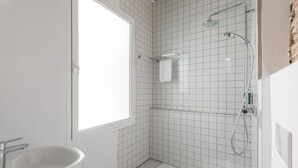 A modern bathroom with a white sink, a shower with a handheld showerhead, and a window providing natural light. - Superior Suite - Open Space (Sevilla)