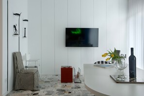 A modern living room with a TV, a striped chair, a red cabinet, a glass vase with flowers, and a wine bottle. - Room 'Camera Deluxe Fuoco' with Mountain View, Wi-Fi and Air Conditioning (Pompei)