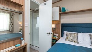 A compact bedroom with a bed, bedside table, and a small desk area. - Waterside Haven (Northampton)